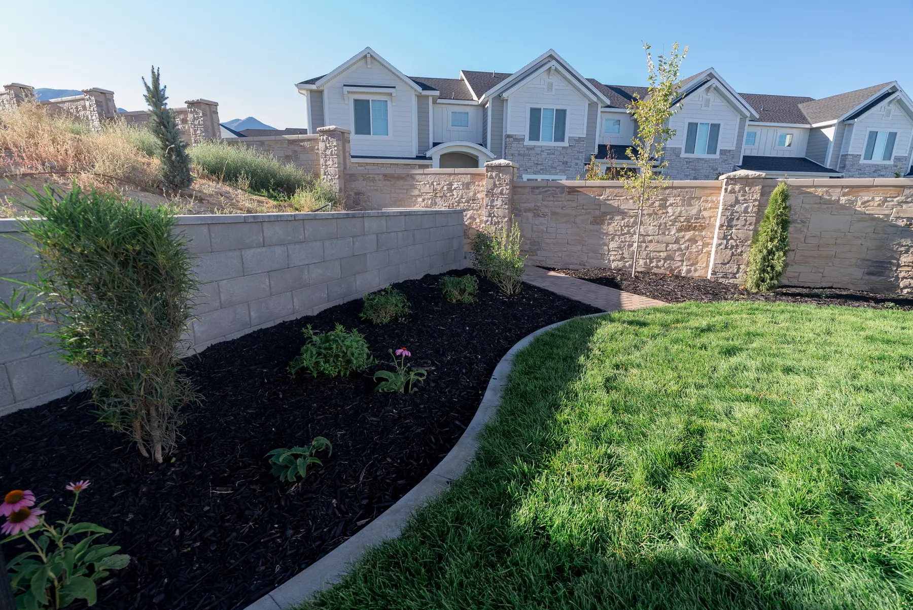 Backyard beds along a stone wall by J&H Landscaping in Spanish Fork