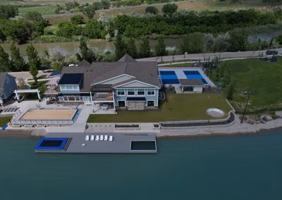 Aerial view of a large residential property with landscaped yard, swimming pools, and a dock along a river, showcasing J&H Landscaping's design and installation services in Provo, UT.