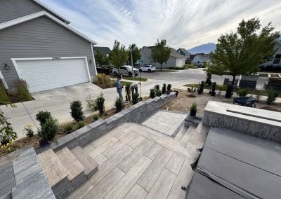 Landscaping project by J&H Landscaping in Provo, featuring newly installed stone steps, plants, and workers enhancing outdoor space.