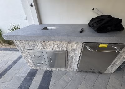 Outdoor kitchen countertop featuring a sink, storage drawers, and refrigerator, showcasing J&H Landscaping's custom landscaping and hardscaping work in Provo, UT.
