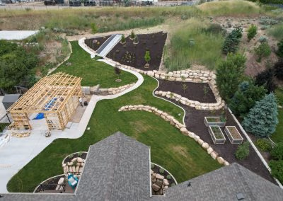 Aerial view of a landscaped yard featuring curving pathways, a wooden structure, and stone borders, showcasing J&H Landscaping's design expertise in Provo, UT.