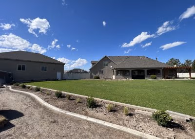 Lush green lawn and landscaped garden featuring a curved pathway, showcasing a residential property by J&H Landscaping in Provo, UT.