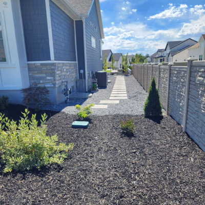 Landscaped pathway alongside a home in Lindon, Utah, featuring stone pavers, decorative plants, and gravel, showcasing J&H Landscaping's quality yard design and maintenance services.