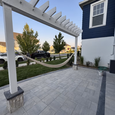 Hammock suspended under a white pergola on a stone patio, surrounded by landscaped greenery and residential homes, illustrating outdoor living space ideal for Mapleton, Utah.