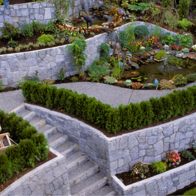 Landscaped garden featuring stone retaining walls, tiered flower beds, a pond, and lush greenery, illustrating high-quality hardscaping and outdoor design suitable for Mapleton properties.