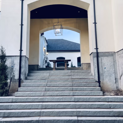 Stone steps leading to an arched entrance, featuring a hanging lantern, framed by walls and greenery, illustrating high-quality hardscaping in a residential setting in Mapleton.